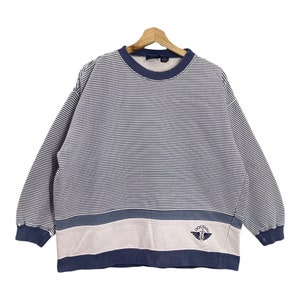 May include: A blue and white striped long-sleeve sweatshirt with a blue and white striped band at the bottom. The sweatshirt has a pink band with a blue "Dockers" logo.