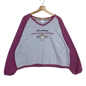May include: A grey sweatshirt with a V-neck and long, deep purple sleeves. The front of the sweatshirt features the text "Grumpy ORIGINAL MINER" with an image of Grumpy from Snow White and the Seven Dwarfs.