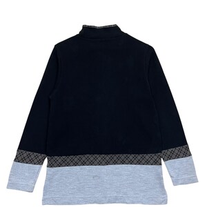 May include: A black long-sleeved shirt with a mock neck and a gray and black plaid pattern at the hem and cuffs. The lower portion of the shirt is light gray.