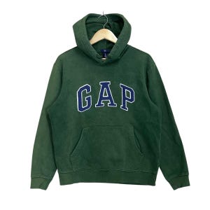 Op de afbeelding: Een groene hoodie met een donkerblauw "GAP" logo op de voorkant.