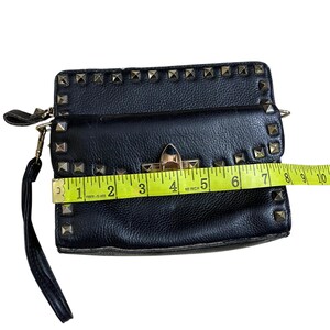 May include: Black clutch with gold-colored studs and hardware. The clutch is approximately 9 inches wide. It has a wrist strap and a clasp closure. The material appears to be leather or a leather-like material.
