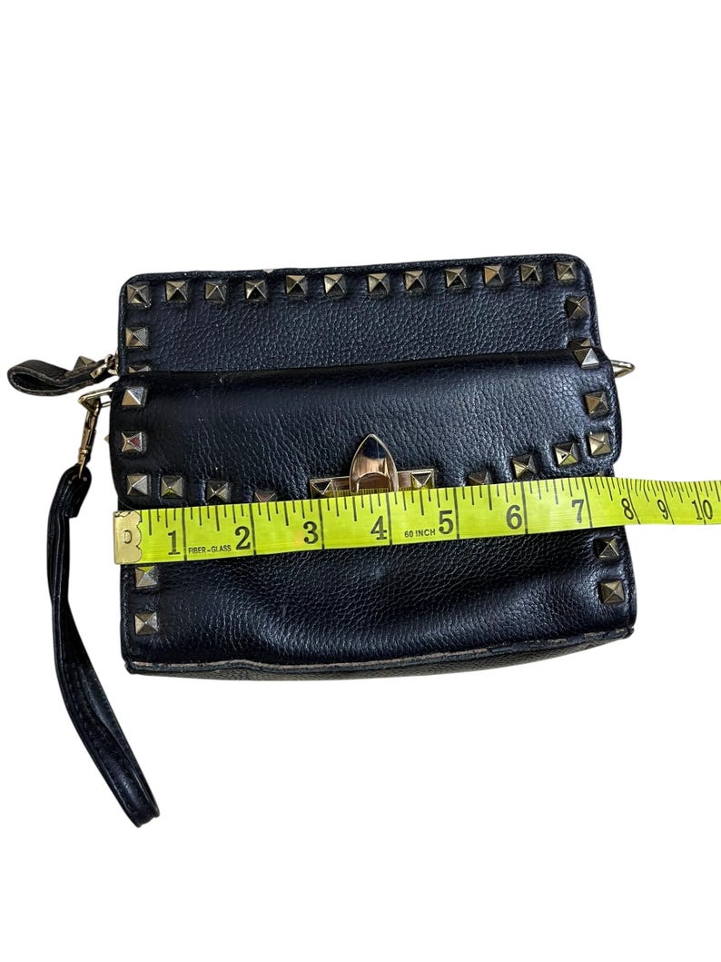 May include: Black clutch with gold-colored studs and hardware. The clutch is approximately 9 inches wide. It has a wrist strap and a clasp closure. The material appears to be leather or a leather-like material.