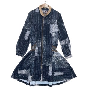 May include: A long-sleeved, patchwork denim dress with a brown corduroy collar and a full-length zip. The dress features a fitted waist with brown elastic detailing and a flared skirt. The fabric has a faded, distressed appearance.