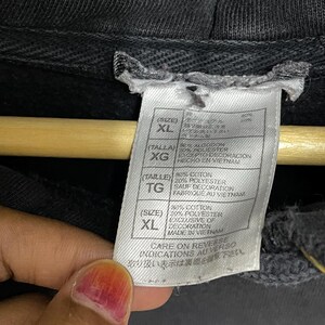 Puede incluir: Una sudadera con capucha negra con una etiqueta blanca que dice "(Size) XL 30% Algod&oacute;n 20% Poli&eacute;ster Exclusivo de Decoraci&oacute;n Hecho en Vietnam" y "Care on Reverse Indications au Verso"