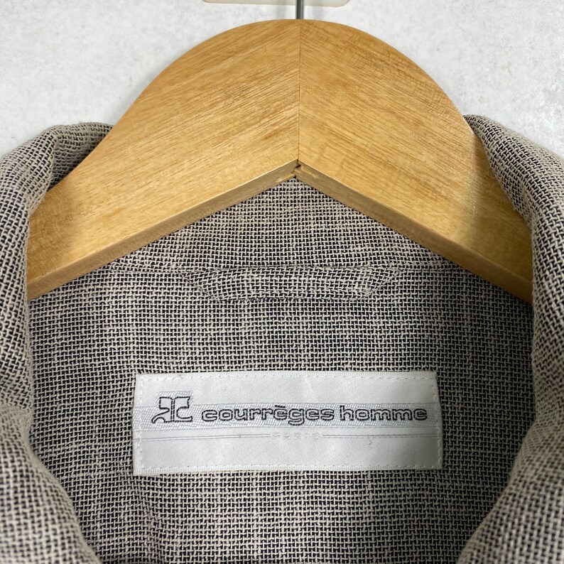 May include: A close-up of a beige linen shirt with a white label that reads "courr&egrave;ges homme".