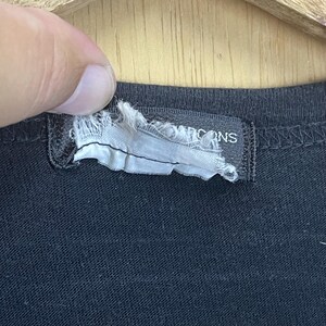 May include: Close-up of a black t-shirt with a white tag that reads "Icons" in black text.