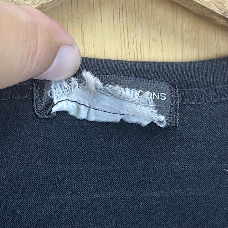 May include: Close-up of a black t-shirt with a white tag that reads "Icons" in black text.
