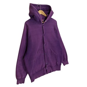 May include: A deep purple hooded sweatshirt with a button-up front and two front pockets. The sweatshirt is hanging on a wooden hanger. The fabric appears to be a soft, worn material.