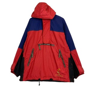 May include: A red, blue, and black anorak jacket with a hood. The jacket has a half-zip closure, two side pockets, and a small embroidered design on the front. The brand name "DESCENTE" is visible on the zippers.