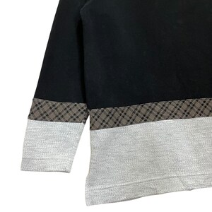 May include: Black and gray sweatshirt with a geometric pattern. The top portion is black, with a brown and gray patterned band separating it from the gray bottom. The sleeves are black with a gray cuff.