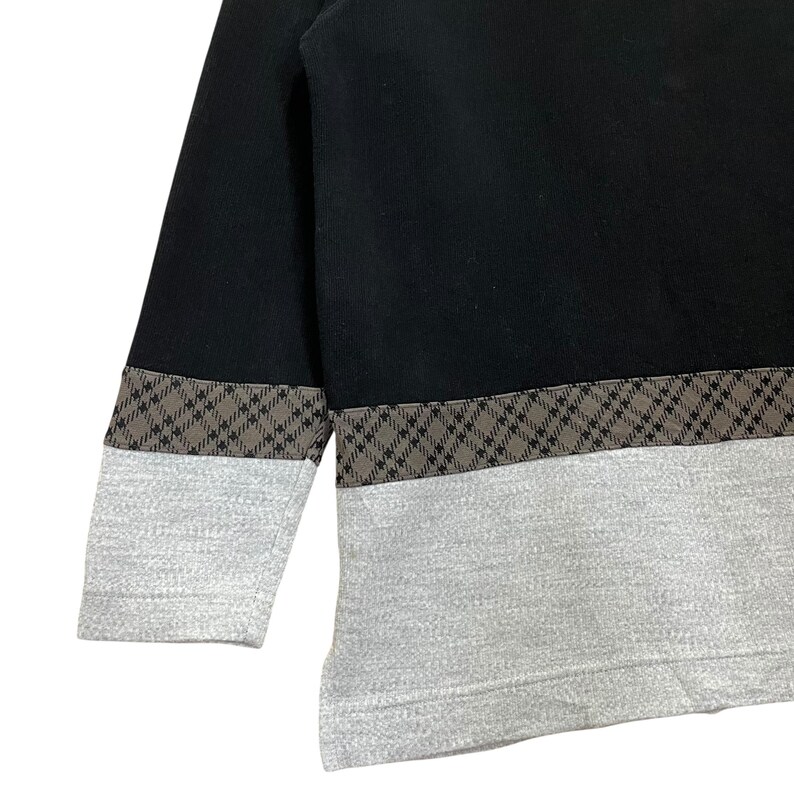 May include: Black and gray sweatshirt with a geometric pattern. The top portion is black, with a brown and gray patterned band separating it from the gray bottom. The sleeves are black with a gray cuff.