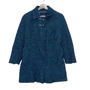 Puede incluir: Un abrigo de tweed azul verdoso con cierre de botones y un pequeño bolsillo en el lado izquierdo. El abrigo tiene una etiqueta que dice "Sport Max Code".