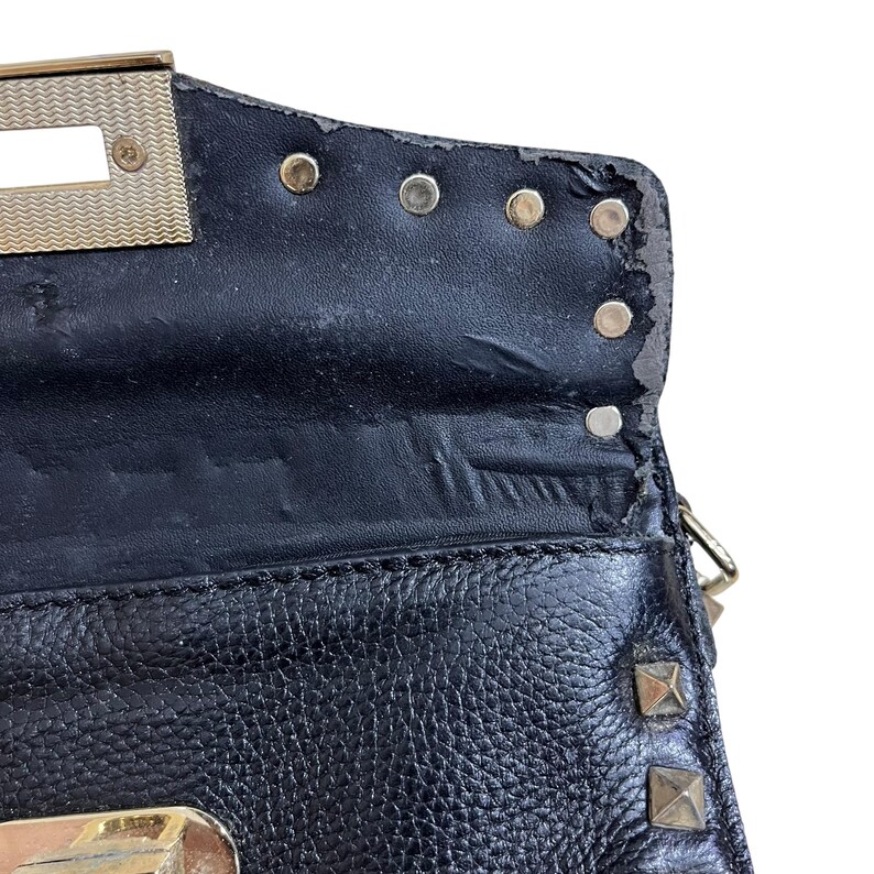 May include: Close-up of a black leather handbag with gold-colored hardware. The bag features a textured surface, metal studs, and a clasp. The top edge shows some wear and tear.
