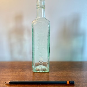 K&ouml;nnte beinhalten: Eine klare Glasflasche mit strukturierter Oberfl&auml;che. Die Flasche ist mit dem Text "E.S. & C.Y. COFFEE & CHICORY" gepr&auml;gt.