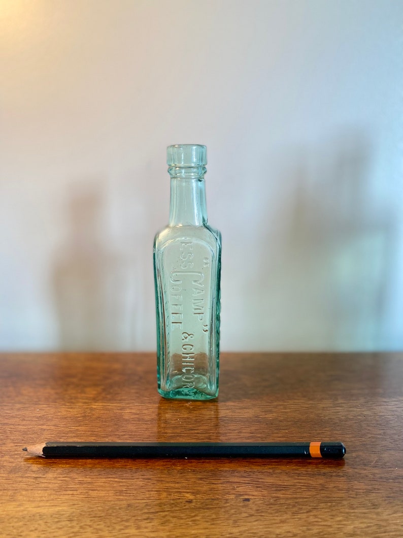 K&ouml;nnte beinhalten: Eine klare Glasflasche mit strukturierter Oberfl&auml;che. Die Flasche ist mit "YAMP. COFFEE & CHICORY" beschriftet.