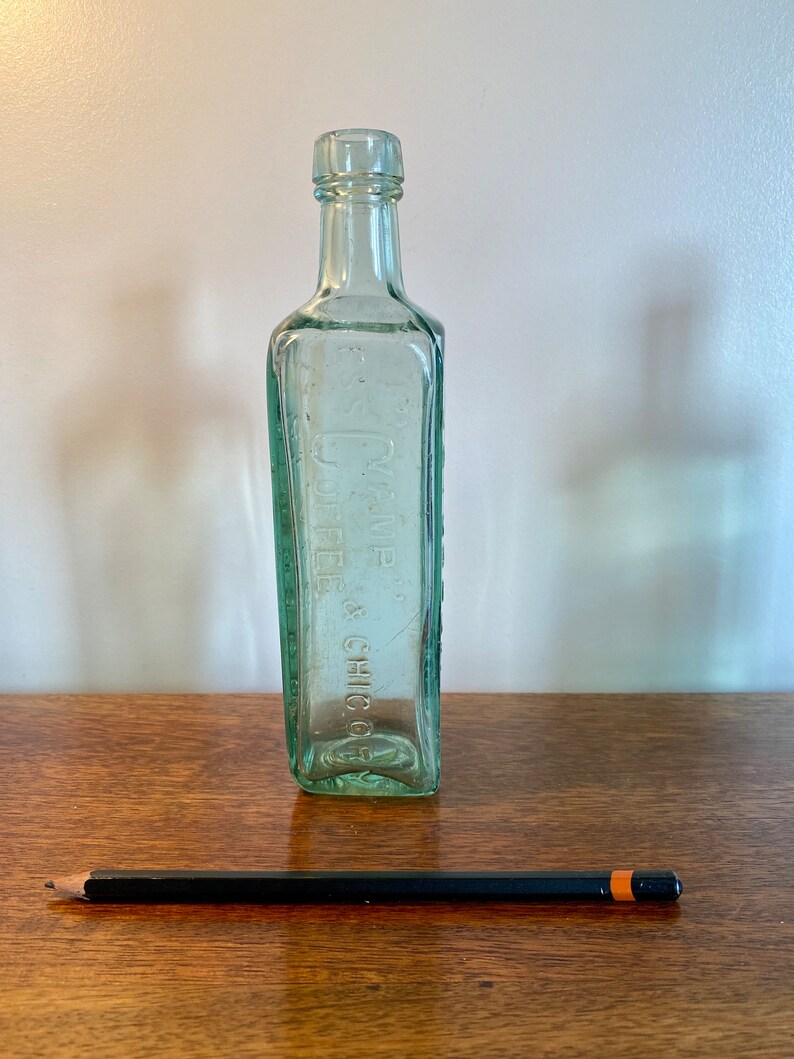 K&ouml;nnte beinhalten: Eine durchsichtige Glasflasche mit quadratischer Form und einer strukturierten Oberfl&auml;che. Die Flasche tr&auml;gt ein Etikett mit der Aufschrift "D.W. DYE & CHIC. CO."