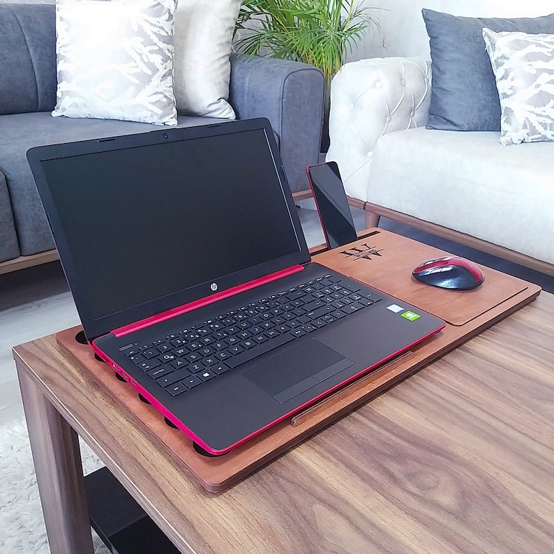 Op de afbeelding: Een houten laptoptafel met een zwarte en rode HP laptop, een rode en zwarte muis en een smartphone. De tafel heeft een ingebouwde telefoonhouder en muismat. De laptop is open en toont een zwart scherm.