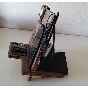 May include: A wooden organizer with slots for a phone, watch, glasses, and keys. The organizer is made of dark wood and has a natural finish.