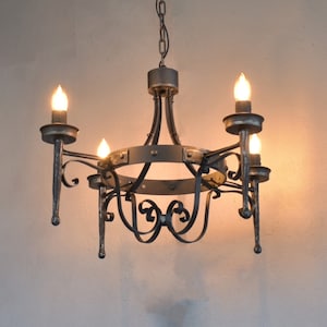 Pode incluir: Um lustre de metal cinza-escuro com uma estrutura circular e quatro luzes em formato de vela. A estrutura inclui braços de metal curvos e volutas decorativas, suspenso por uma corrente de metal correspondente fixada ao teto.