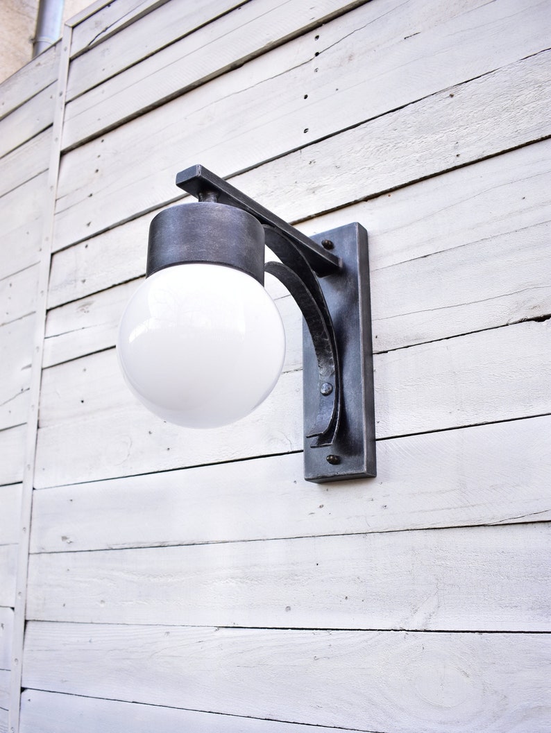 A black metal outdoor wall light fixture with a white glass globe light bulb