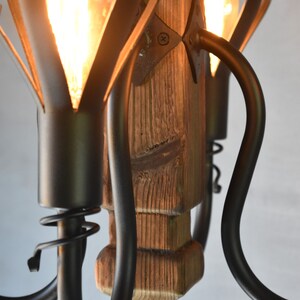 May include: A rustic wooden chandelier with black metal arms and light bulbs. The chandelier has a unique design with the arms curving up and out.