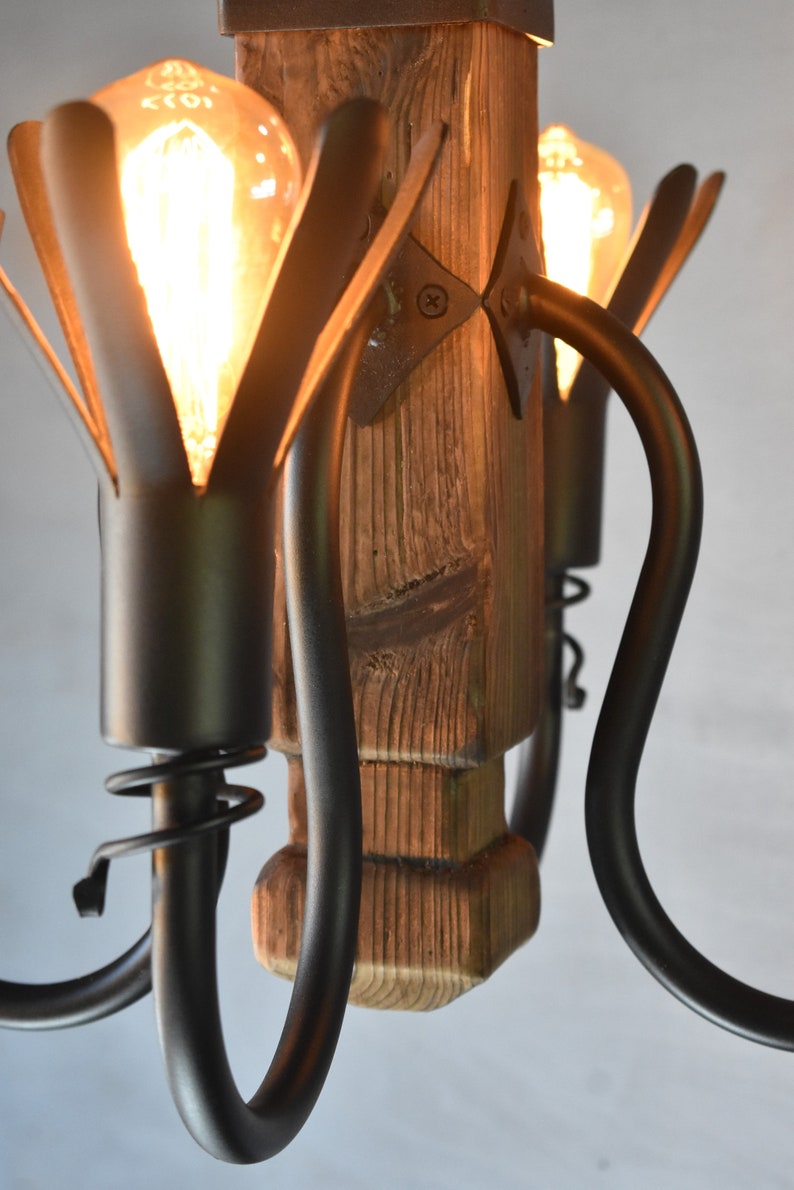 May include: A rustic wooden chandelier with black metal arms and light bulbs. The chandelier has a unique design with the arms curving up and out.