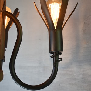 May include: A black metal chandelier with a wooden base and multiple light bulbs. The light bulbs are encased in a black metal flower-shaped fixture.