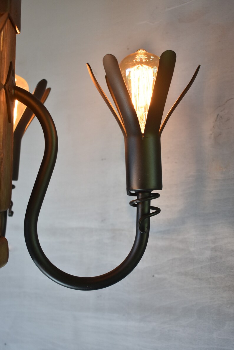 May include: A black metal chandelier with a wooden base and multiple light bulbs. The light bulbs are encased in a black metal flower-shaped fixture.