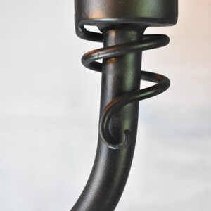 May include: Close-up of a black metal light fixture with a decorative spiral detail. The fixture is made of a smooth, black metal and has a simple, elegant design.