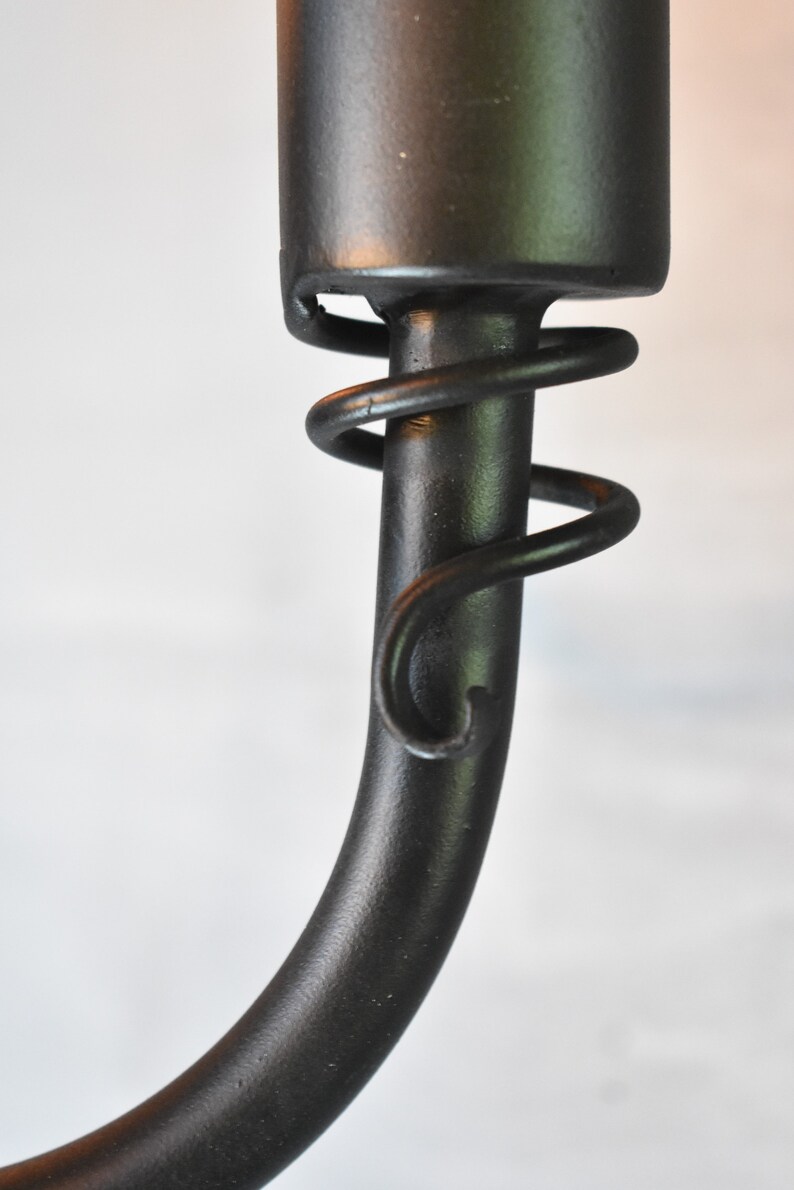 May include: Close-up of a black metal light fixture with a decorative spiral detail. The fixture is made of a smooth, black metal and has a simple, elegant design.