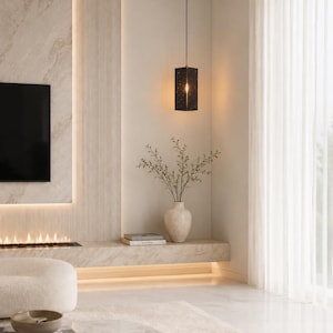 May include: A rectangular black pendant light with a perforated star pattern hangs from a thin cord. The fixture emits a warm glow, illuminating the surrounding cream-colored wall and a white ceramic vase filled with thin, leafy branches.