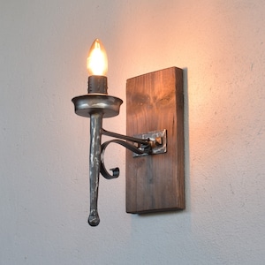 Pode incluir: Uma arandela de parede rústica com uma única lâmpada. A arandela é feita de metal e tem uma base de madeira. A lâmpada é uma lâmpada incandescente tradicional.