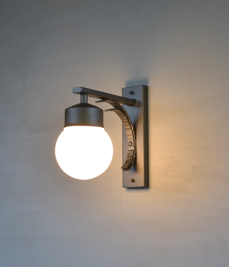 A black metal wall sconce with a white glass globe light bulb. The sconce has a curved arm and a rectangular base.