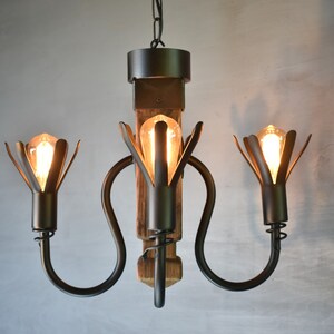May include: A black metal chandelier with three lights, each with a flower-shaped shade. The chandelier is made of reclaimed wood and has a rustic look.