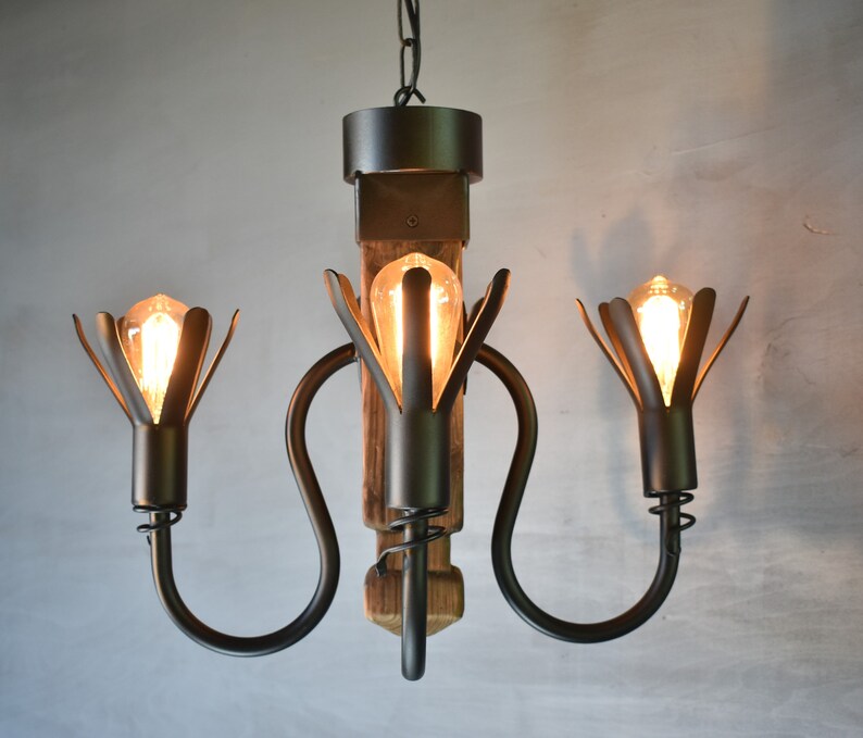 May include: A black metal chandelier with three lights, each with a flower-shaped shade. The chandelier is made of reclaimed wood and has a rustic look.