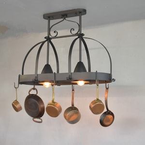 May include: Black wrought iron pot rack with three lights and six hooks holding copper pots and pans.
