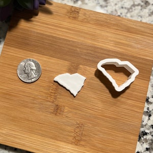 May include: Two white plastic cookie cutters shaped like the state of South Carolina. The larger cutter is about the size of a US quarter.