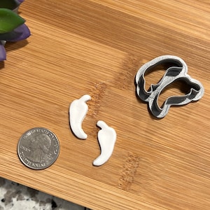 May include: Two white plastic chili pepper cookie cutters and a silver metal chili pepper cookie cutter on a wooden surface.