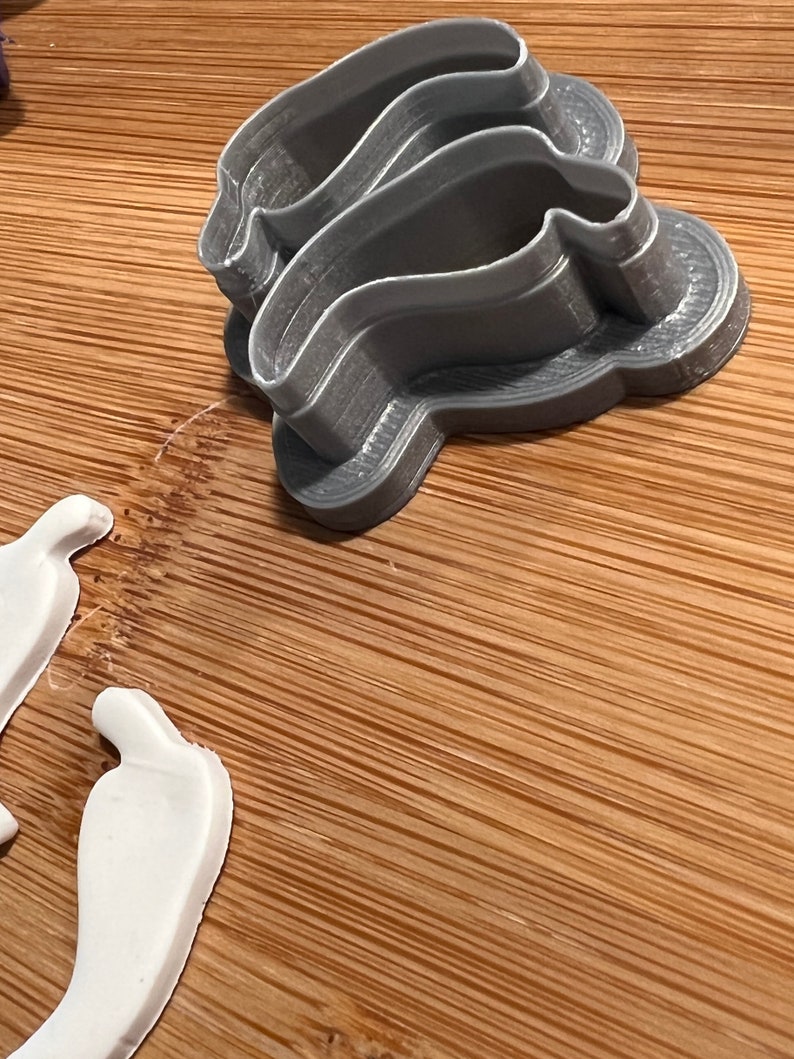 May include: A set of three gray plastic cookie cutters shaped like a chili pepper. The cutters are stacked on top of each other.