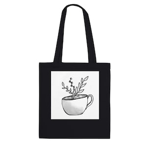 Könnte beinhalten: Eine schwarze Tragetasche mit einer zentrierten weißen quadratischen Grafik. Die Grafik zeigt eine schwarz-weiße Strichzeichnung einer Teetasse, die mit einem blättrigen Pflanzensprössling mit kleinen Beeren gefüllt ist, in einem schlichten Stil.