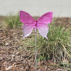 Könnte beinhalten: Ein rosafarbener und weißer Schmetterlings-Gartenpfahl mit einem Stiel aus Metall. Der Schmetterling ist aus Kunststoff und hat ein Farbverlauf-Design.
