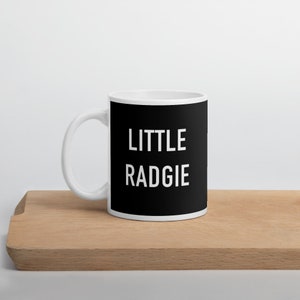 May include: White ceramic mug with a black design. The text "LITTLE RADGIE" is printed in white on the black background.