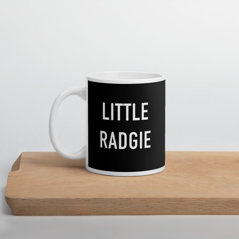 May include: White ceramic mug with a black design. The text "LITTLE RADGIE" is printed in white on the black background.