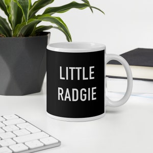 May include: White ceramic mug with a black background and the text "LITTLE RADGIE" in white.