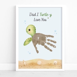 May include: A framed print featuring a handprint turtle design with the text "Dad I Turtle-y Love You." The turtle has a green head and flippers, with a brown handprint body. The background is light blue with sand and seashells.