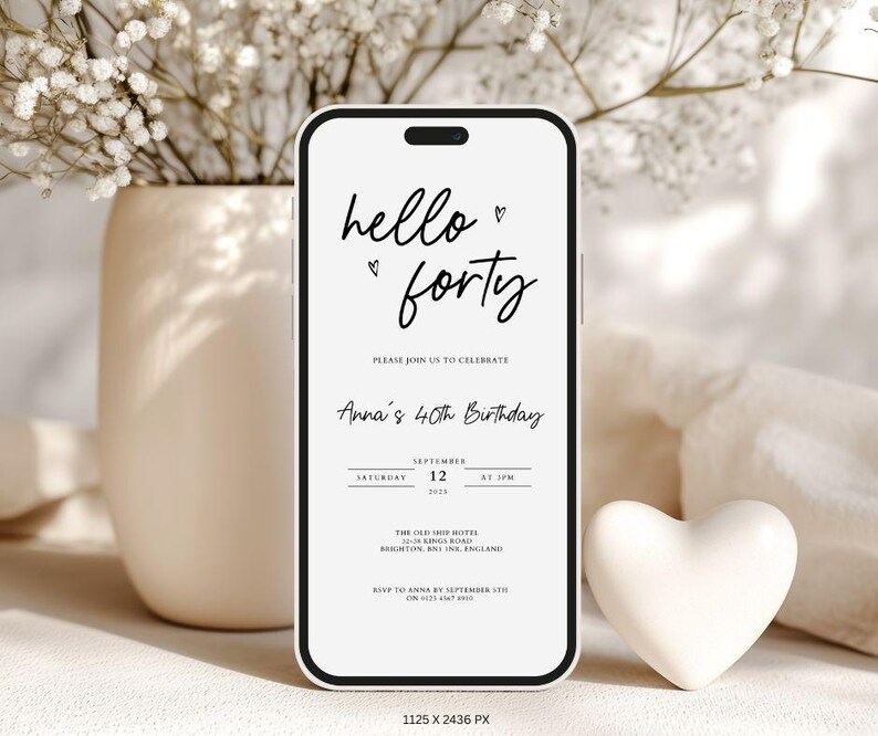 May include: A smartphone displays a birthday invitation with the words "hello forty" in elegant script. The invitation includes details for Anna's 40th birthday, with a heart symbol. A white heart-shaped decoration sits beside the phone.