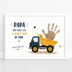 Könnte beinhalten: Ein gerahmter Druck mit einer Illustration eines blauen und gelben Muldenkippers und einem Handabdruck. Der Text lautet "PAPA, you make life a whole load of fun!" und "Happy Father's Day". Der Druck hat einen weißen Rand.