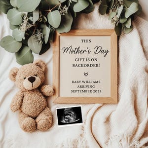 Könnte beinhalten: Ein gerahmter Holzrahmen mit dem Text "This Mother's Day Gift is on Backorder!" und "Baby Williams Arriving September 2025." Ein Teddybär und ein Ultraschallbild befinden sich neben dem Rahmen. Eukalyptusblätter sind im Hintergrund.
