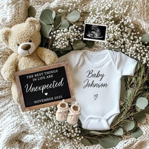 May include: A baby announcement with a teddy bear, a chalkboard sign, a white babygrow, baby booties, and an ultrasound scan. The chalkboard reads "The Best Things in Life Are Unexpected November 2025". The babygrow says "Baby Johnson".