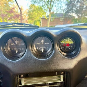 May include: A black dashboard featuring three circular gauges. The left gauge displays temperature and oil pressure. The center gauge shows amperage and fuel levels. The right gauge is a digital AEM air/fuel ratio display with red text.